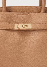 Τσάντα χειρός από ανοιχτό καφέ δέρμα με υφή, δύο κοντές λαβές και κλείσιμο με χρυσό μεταλλικό κουμπί.