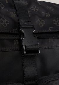 Zwarte nylon tas met een textuurpatroon van bloemen en letters. Hij is voorzien van een plastic gesp met het merk "JOOP!" en stevige banden.