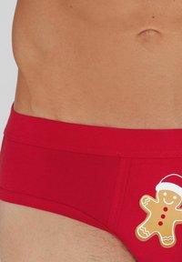 Roter Baumwoll-Slip mit einem Lebkuchenmann-Motiv, der einen Weihnachtsmannhut trägt. Glatte Textur und elastischer Bund, für einen bequemen Sitz entworfen.