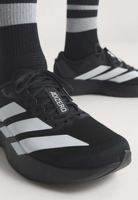 Scarpe da corsa Adidas Adizero bianche e nere indossate con calzini neri con righe bianche e grigie.