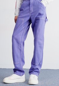Purple cargo pants made of durable fabric with contrast stitching; feature side pockets and a relaxed fit, paired with white sneakers.