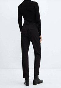 Pantalons noirs ajustés en tissu lisse, présentant une coupe droite et des poches passepoilées au dos, associés à des bottines noires.