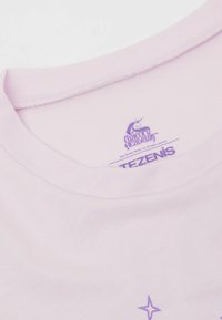 Hellrosa Baumwoll-T-Shirt mit Rundhalsausschnitt. Mit lila Text und einem Einhorn-Motiv auf dem inneren Etikett, glatte Textur.