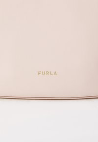 Bolso de mano de cuero color rosa con un acabado texturizado, que presenta un detalle de logotipo dorado que dice "FURLA" en la parte inferior del frente. Diseño limpio y minimalista.