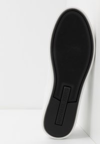 Semelle de chaussure avec grip texturé noir et marque Michael Kors en noir, contrastant avec des bords de chaussure blancs sur un fond blanc.