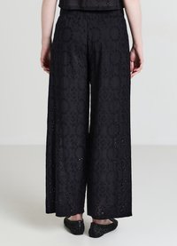 Schwarze, weit geschnittene Hosen aus besticktem Stoff mit kreisförmigen und floralen Mustern, mit strukturierter Optik und elastischem Bund.