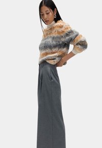 Kraftig strikket sweater i orange, grå og cremefarvede striber; grå højtaljede bukser med vide ben; glat, struktureret stof; lange ærmer.