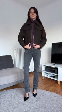 Jachetă scurtă maro cu două buzunare frontale, purtată peste un pulover cu guler înalt mov, asortată cu blugi gri și pantofi cu toc negri, vârf ascuțit.