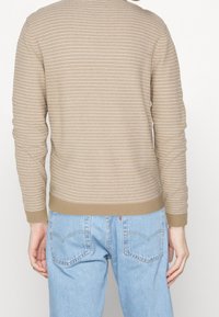 Beige randig tröja med långa ärmar, ribbade manschetter och nederdel. Matcher med ljusblå denim jeans som visar en avkopplad passform.