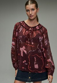 Gennemsigtig bordeaux-bluse med en flæsekrave, snører detaljer og legende mønstre af flasker, sløjfer og kirsebær. 