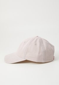 Light pink baseball cap made of textured fabric, featuring a curved visor, six-panel design, and an embroidered logo on the side.