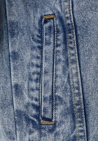 Denim tkanina u svijetloplavoj boji s teksturiranim izgledom. Ima pravokutnu petlju i kontrastne žute šavove duž rubova.