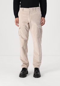 Beige corduroy cargo bukser med struktureret stof, to sidelommer og en knaplukning. Stylede med sorte sko og en sort top.