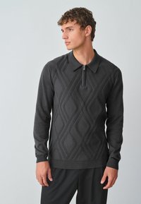 Sötét szürke pulóver zipzáras gallérral, textúrált gyémántmintákkal és hosszú ujjal. Puha, kötött anyagból készült.