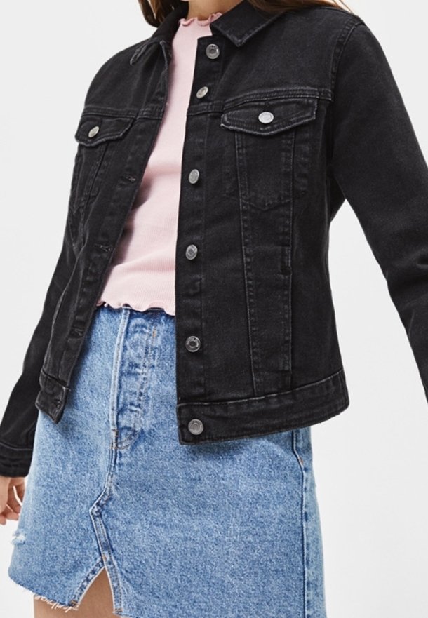 Svart denimjacka med krage, främre fickor med lock, silverdetaljer och knappstängning, bärs över en rosa ribbad topp och en denimkjol.