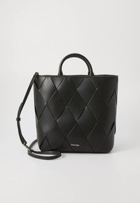 Black leather tote bag with a woven design, featuring a top handle and a detachable shoulder strap. Calvin Klein logo on the front.