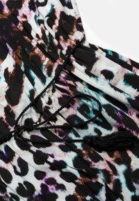 Tissu en imprimé animal multicolore avec un cordon noir froncé noué en nœud et des glands, mettant en valeur les détails de texture et de motif.