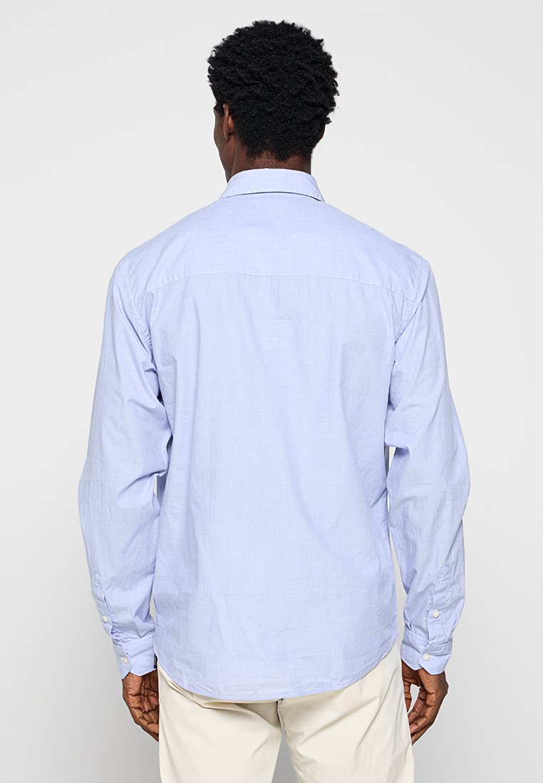 Camicia a maniche lunghe di colore azzurro chiaro, realizzata in cotone, con colletto a punta, dettaglio della yoke posteriore e polsini con bottoni. Tessuto liscio.
