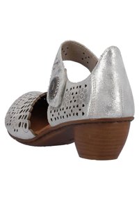 Zapato de cuero plateado cortado con punta redonda y bajo tacón de madera. Presenta un prominente botón decorativo en el lado.