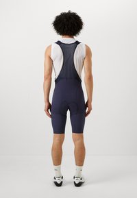 Shorts da ciclismo di colore blu navy con schiena in rete, dotati di imbottitura e vestibilità aderente. Il design enfatizza funzionalità e comfort per il ciclismo.