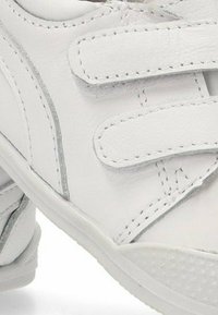 Zapatilla de cuero blanca con tiras de velcro, acentos plateados y suela de goma texturizada. Punta redondeada y cuello acolchado para mayor comodidad.