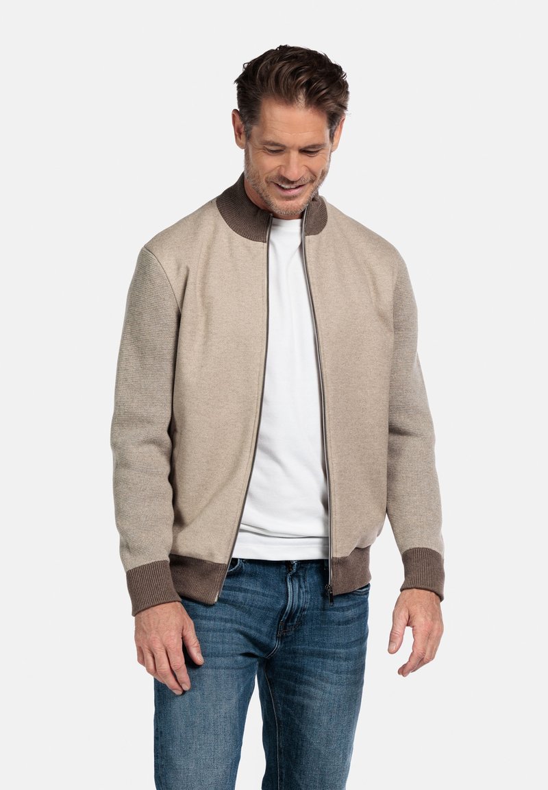 Khaki Bomberjacke mit einem braunen gerippten Kragen und Bündchen. Das Material hat eine glatte Textur. Verfügt über einen durchgehenden Reißverschluss und Seitentaschen.