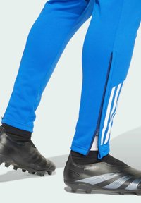 Blauwe sportieve joggerbroeken met ritsen op de enkels, gecombineerd met zwarte voetbalschoenen met textuur en zilveren accenten.