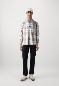 Knappe rutete skjorte i hvitt, beige og brunt, med brystlomme, kombinert med mørk denimjeans og beige sneakers. Glatt stofftekstur.