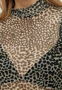 Sheer toppi, jossa on monivärinen leopardi-printtikuvio beigen, ruskean ja mustan sävyissä. Siinä on korkea kaula-aukko ja teksturoitua kangasta.