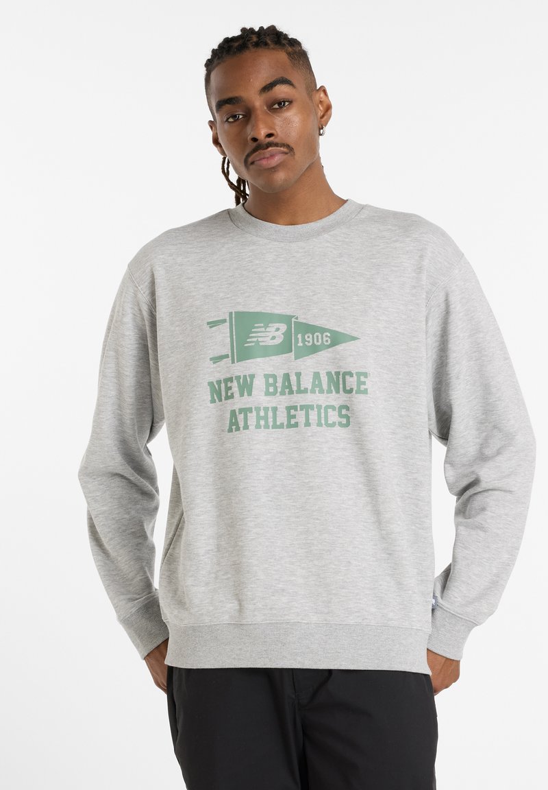 Grå sweatshirt tillverkad av bomullsblandning. Har grön grafisk text "NEW BALANCE ATHLETICS" och en flaggdesign. Ribbad mudd och nederkant.