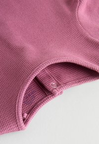 Rosa strukturierter Stoff mit einem gerippten Design, ausgestattet mit einem runden Ausschnitt und einem kleinen Metallschmuckdetail an der Öffnung.
