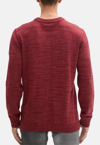 Pull en laine rouge avec un motif texturé, col rond et manches longues. Le tissu semble doux ; la vue de dos montre une coupe décontractée.
