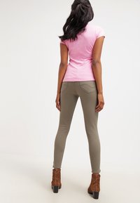 Różowa koszulka z krótkim rękawem połączona z dopasowanymi oliwkowymi spodniami oraz brązowymi botkami za kostkę. Stylizacja ma swobodny, smukły kształt.