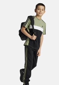 Conjunto deportivo en negro y verde oliva con una camiseta de bloques de color y pantalones a juego. Presenta tres rayas en los laterales y una mochila.