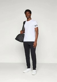 Valge T-särk, mille seeliku peal on must "BO" trükk, on kombineeritud mustade joggerite ja valgete tossudega. Kandas musta õlakotti.