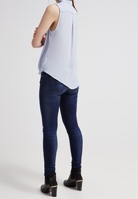 Blusa senza maniche azzurro chiaro con orlo asimmetrico, abbinata a jeans skinny scuri e stivaletti alla caviglia con dettaglio dorato sul tacco.