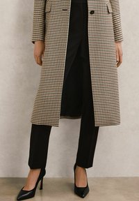 Pruunide ja beežide hundihambamustriga mantel, millel on kohandatud disain, kombineeritud mustade pükste ja mustade kõrge kontsaga kingadega. Üldiselt sujuvad tekstuurid.