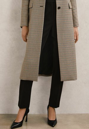 Brun og beige hundetandsmønstret frakke med et skræddersyet design, kombineret med sorte bukser og sorte højhælede sko. Glatte teksturer overalt.