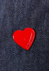 Rött hjärtformat märke av blankt material med texten "LOVE" präglad på ena sidan, placerad mot en jeansbakgrund.
