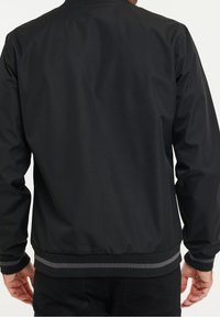 Blouson bomber noir avec une finition mate et lisse. Doté de poignets et d'une taille côtelés avec une bande grise. Design simple et contemporain.