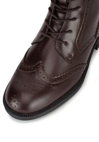 Pruun nahast kleitjalanõu brogue-detailidega, terava ninaga ja lame kummist tallaga. Omadused hõlmavad paelaga kinnitamist ja tekstuuritud aktsente.