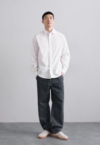 Camisa blanca de botones de manga larga combinada con unos vaqueros grises sueltos y zapatillas blancas. Diseño simple y ajuste relajado.
