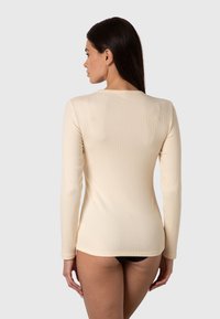 Top a maniche lunghe in beige chiaro, con scollatura dritta e silhouette aderente, abbinato a biancheria intima nera.
