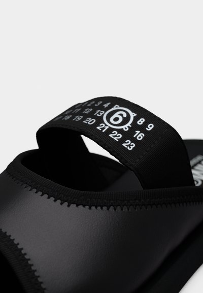 Μαύρο σανδάλι με φαρδιά ραμμένη λουρίδα και μαύρο υφασμάτινο κορδόνι έλξης που φέρει λευκούς τυπωμένους αριθμούς και αριθμό 6 μέσα σε κύκλο.