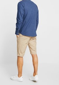 Beiga shorts med fram- och bakfickor, i kombination med en mörkblå långärmad skjorta. Vita sneakers fulländar outfiten.