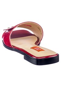 Sandale à glissière en cuir verni rouge avec une semelle intérieure beige lisse et une semelle noire plate. Présente une large bande avec des clous en argent sur le côté.