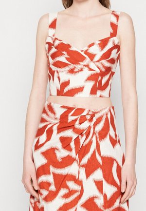 Vrouw draagt een rood-wit patroon crop top met brede bandjes en een bijpassende hoge taille rok met een knoopdetail aan de voorkant.