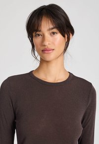 Top maro cu mâneci lungi, realizat din material răsucit, cu decolteu rotund. Prezintă o textură netedă și o siluetă mulată.