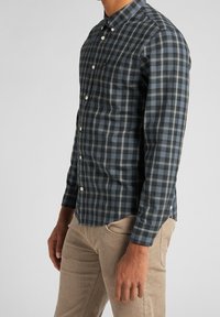 Camicia a quadri con bottoni in blu scuro, nero e bianco. Caratterizzata da maniche lunghe, colletto e orlo arrotondato. Tessuto morbido.