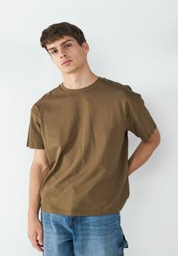 Brown short-sleeve t-shirt made of soft material, featuring a crew neck and relaxed fit, paired with blue denim jeans.